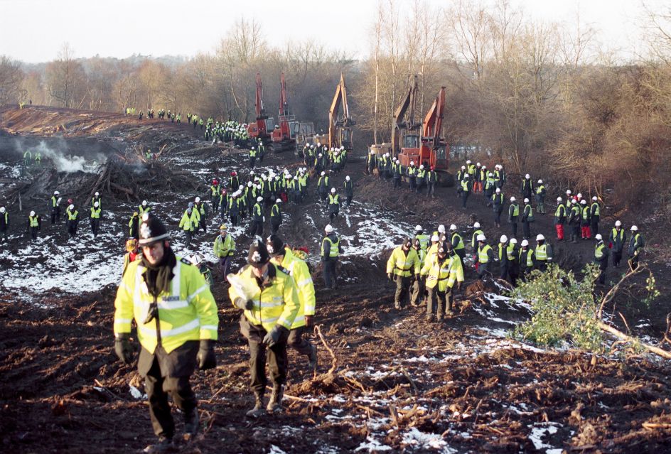 Newbury Bypass 1996 - Much like an army, a line of police and security walk with the diggers in order to ensure activists do not stop them. The overall police and security cost for the entire campaign was £30 million.