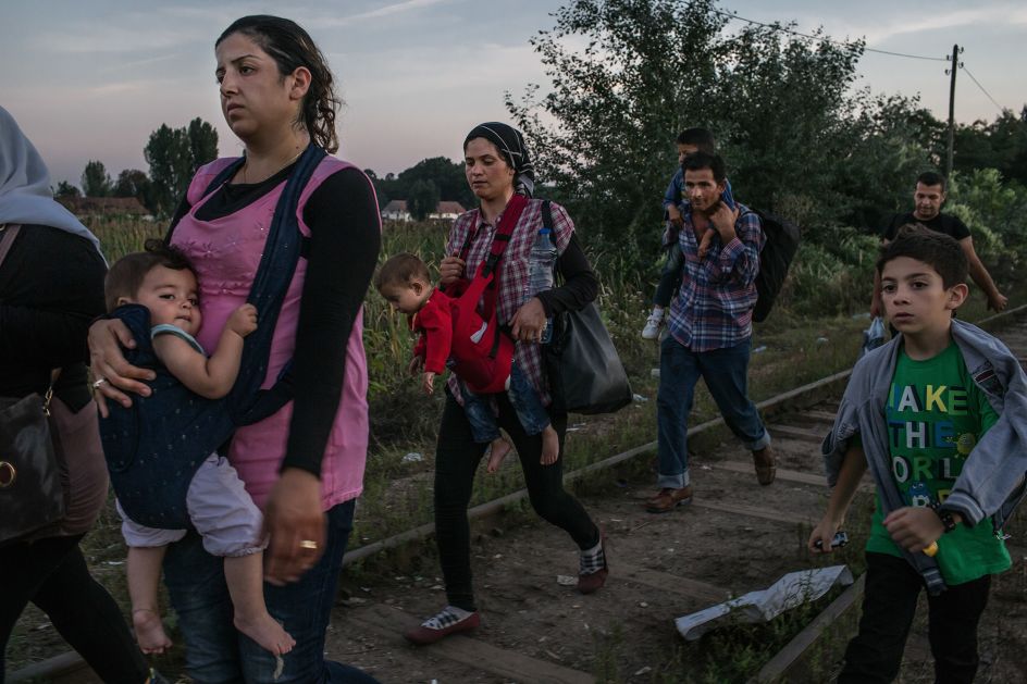 Horgos, Serbia, August 30, 2015. At dusk, Roujin Sheikho, on the left, carries her daughter Widad followed by her son Nabih, on the right. This group walks among other refugees from Syria, who are allowed to cross the barbed wire in the dark into Hungary, on their long road to Sweden. © Mauricio Lima. Documentary Series Winner, Magnum and LensCulture Photography Awards 2016