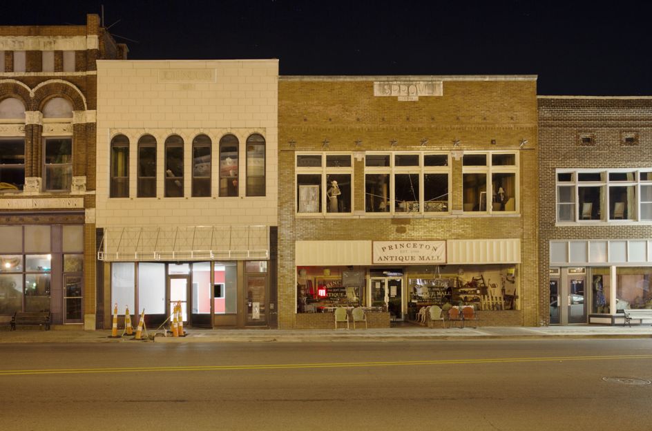 A jigsaw of buildings reveals the goods within and reflect the world outside, peaceful after a day of people staring into them as they pass by.