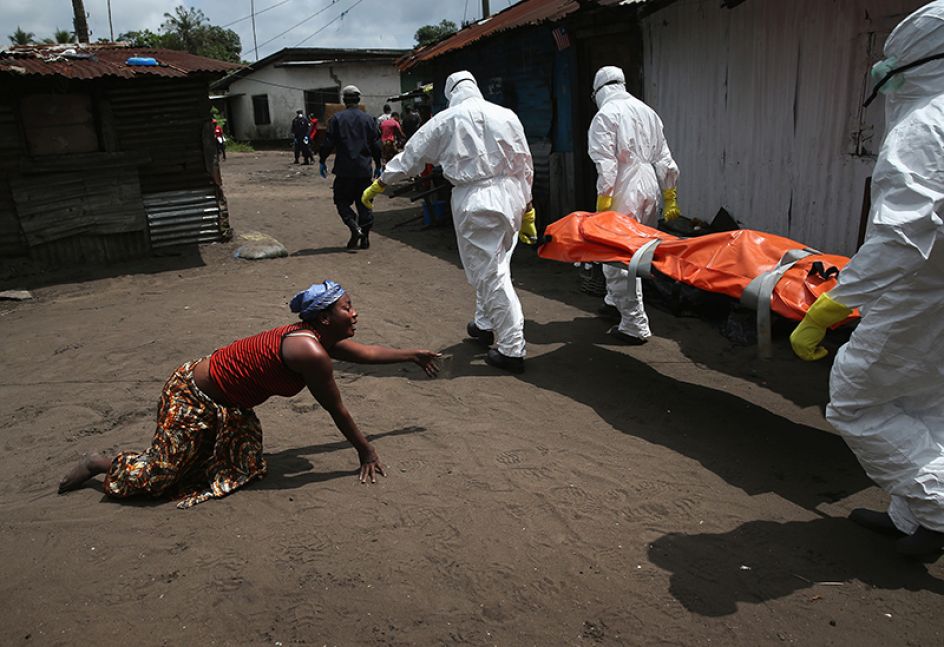 Copyright: John Moore / Getty Images. A woman crawls towards the body of her sister as Ebola burial team members take her away.