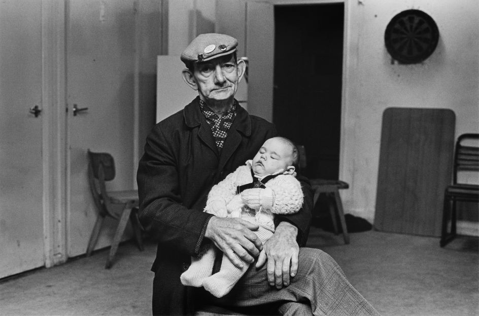 Sidney Richmond, retired Pit Deputy, babysitting Sean (3 months old) – first strike baby in the village. Clipstone Colliery, Nottingham, 1984-85 © Brenda Prince