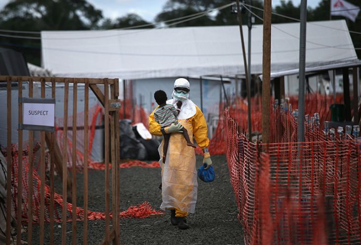 Copyright: John Moore / Getty Images. An MSF health worker in protective clothing carries a sick girl at an Ebola treatment centre.