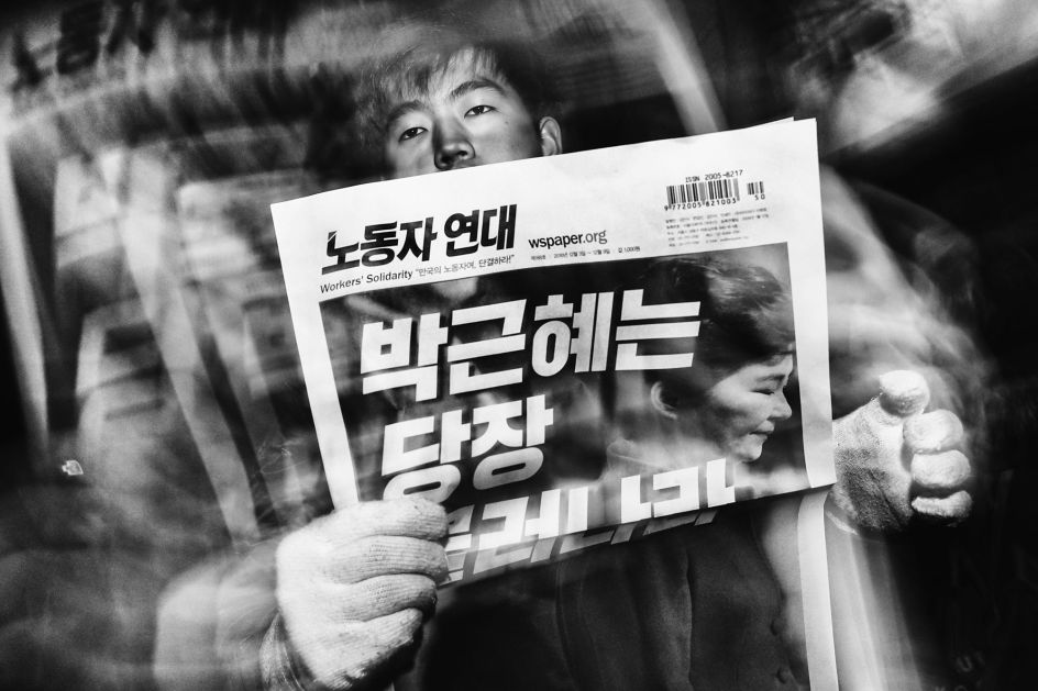 Read All About It. During a cold winter evening, a man sells Workers’ Solidarity newspapers to protesters marching towards the presidential Blue House. The headline reads: ”Park Geun-hye Resign Now.” © Argus Paul Estabrook. Street Series Winner, Magnum and LensCulture Photography Awards 2017