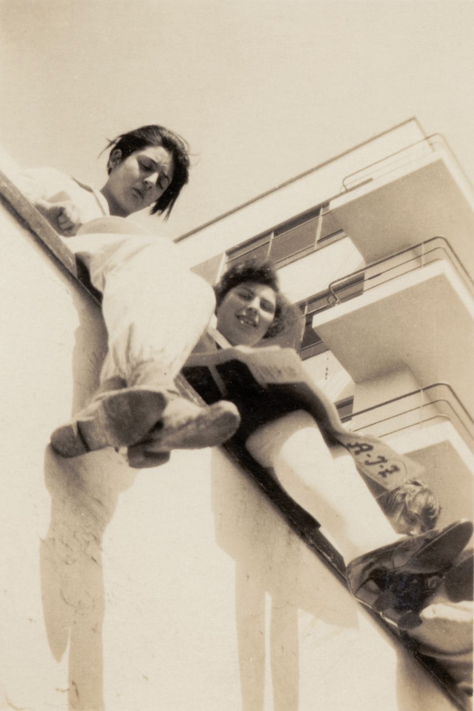 Anonymous: Students on the terrace parapet, Tonja Rapoport with a copy of the AIZ (Arbeiter-Illustrierte-Zeitung) on the Bauhaus balcony, c. 1929. Photo © Bauhaus-Archiv, Berlin