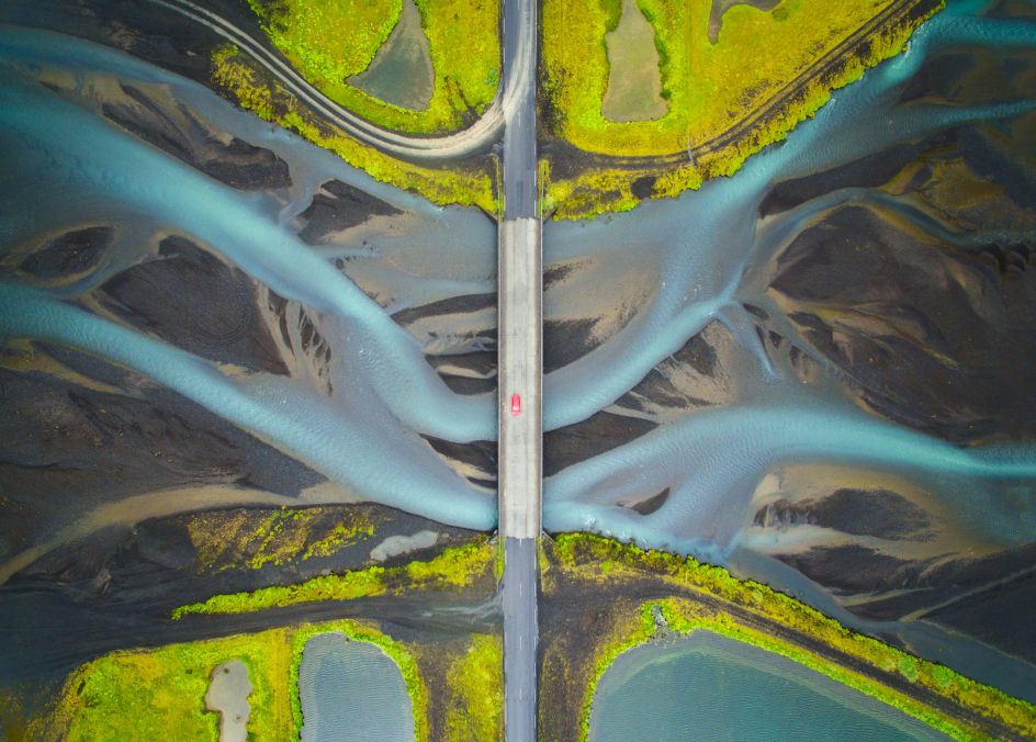 Aerial view of Glacial river in Iceland. While crossing the bridge, I noticed some pattern in the water and wondered how it would look from the sky. I stopped the car at a turnout after crossing the bridge and flew my drone to capture this image. I included the bridge and the car to give an idea of the scale. This river flows to the ocean and becomes part of the sea.  Copyright: © Manish Mamtani, India, Shortlist, Open, Travel (Open competition), 2018 Sony World Photography Awards