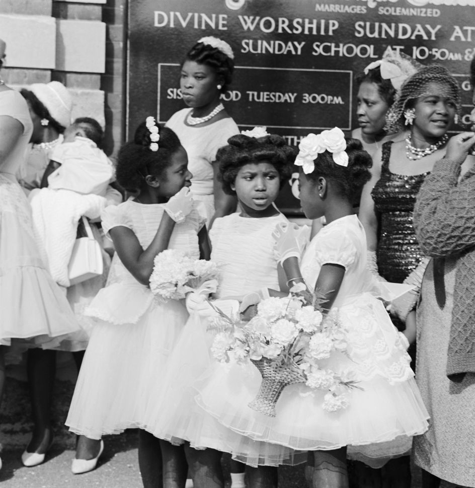 Three young black girls chatting outside a Methodist chapel, 1950-59, © Historic England Archive