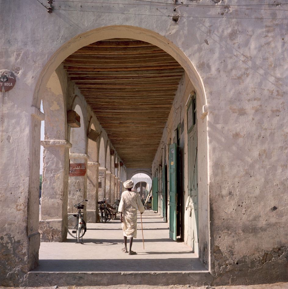 Sudan, 1958 – Man walking by stores along an arched colonnade © 2021 Todd Webb Archive