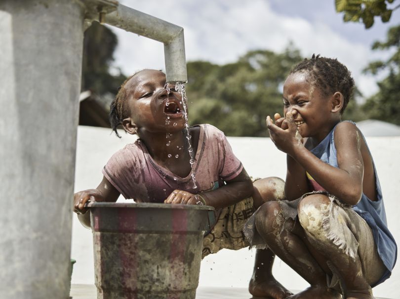 Batu, 10, left, and Madie, 8, play in clean water at the pump in Tombohun, Sierra Leone, May 2017. WaterAid/ Joey Lawrence