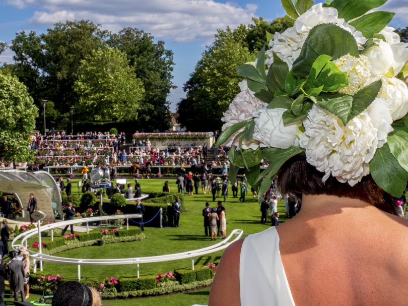A woman in an extravagantly decorated hat looks out across the parade ring on Ladies Day at Royal Ascot. June 2018 © Peter Dench
