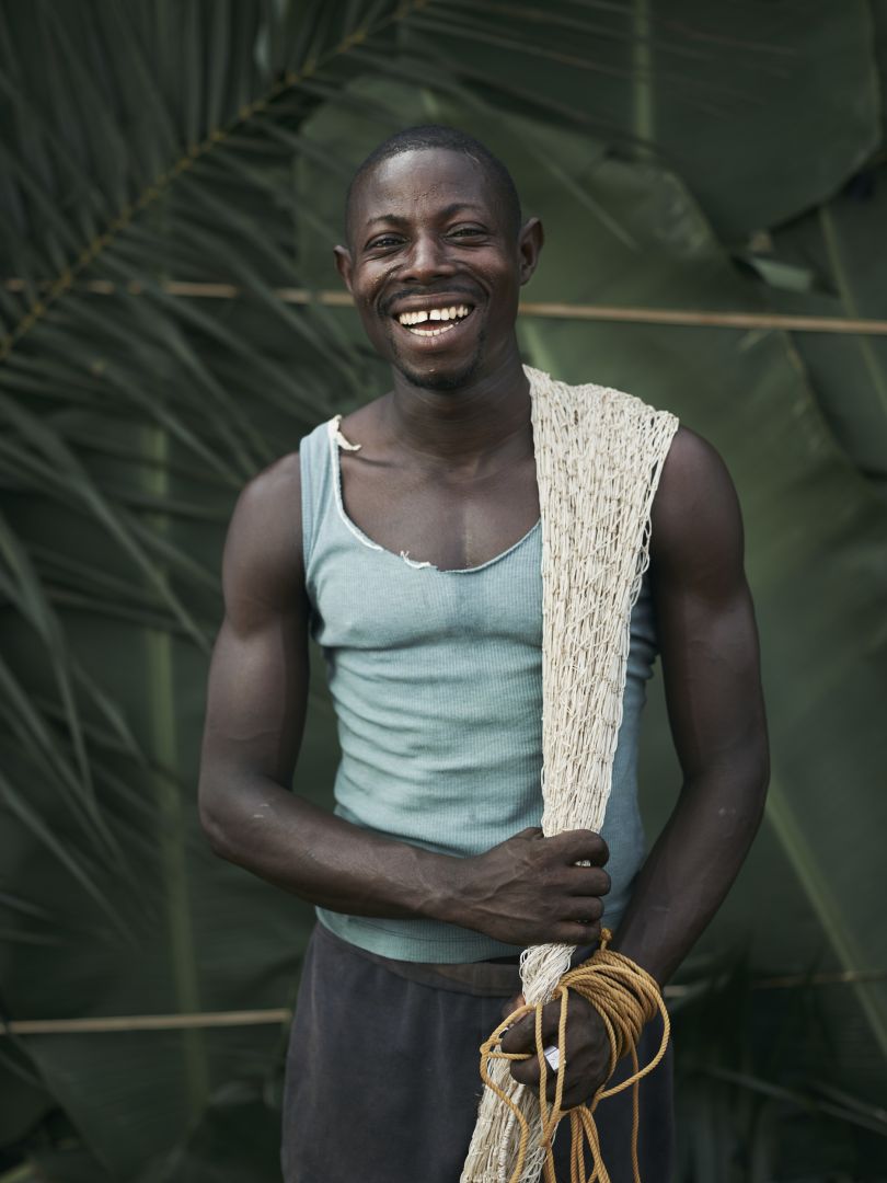 Sellu Smart, holding home-made fishing nets, made from leaves, in the village of Tombohuaun. Sellu spends at least half of his wages on healthcare for his family. If he didn't have to he would develop his farm by increasing the yield, and do more business such as buying palm oil or selling clothes. Kailahun District, Sierra Leone, May 2017. WaterAid/ Joey Lawrence