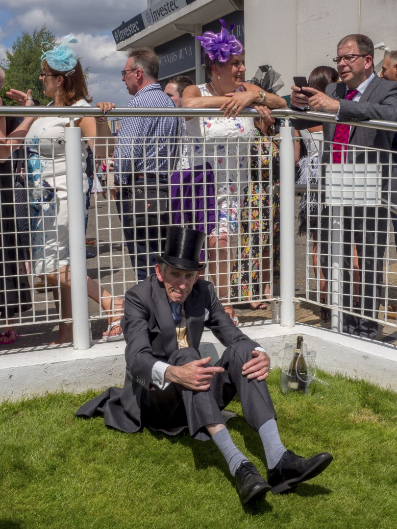 An elderly gentleman in formal attire sat on the grass watching the horse racing from The Queen's Stand during the Epsom festival. June 2018 © Peter Dench