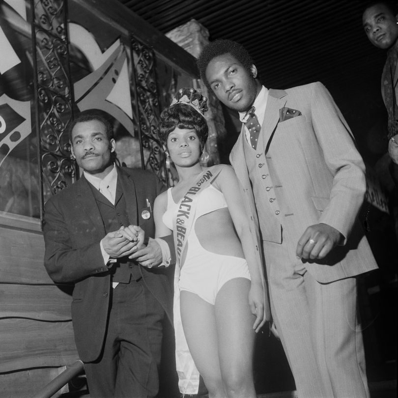 (unidentifed) Miss Black & Beautiful escorted by two men, Hammersmith Palais, London, 1970s. From the portfolio 'Black Beauty Pageants'. © Raphael Albert, courtesy Autograph ABP