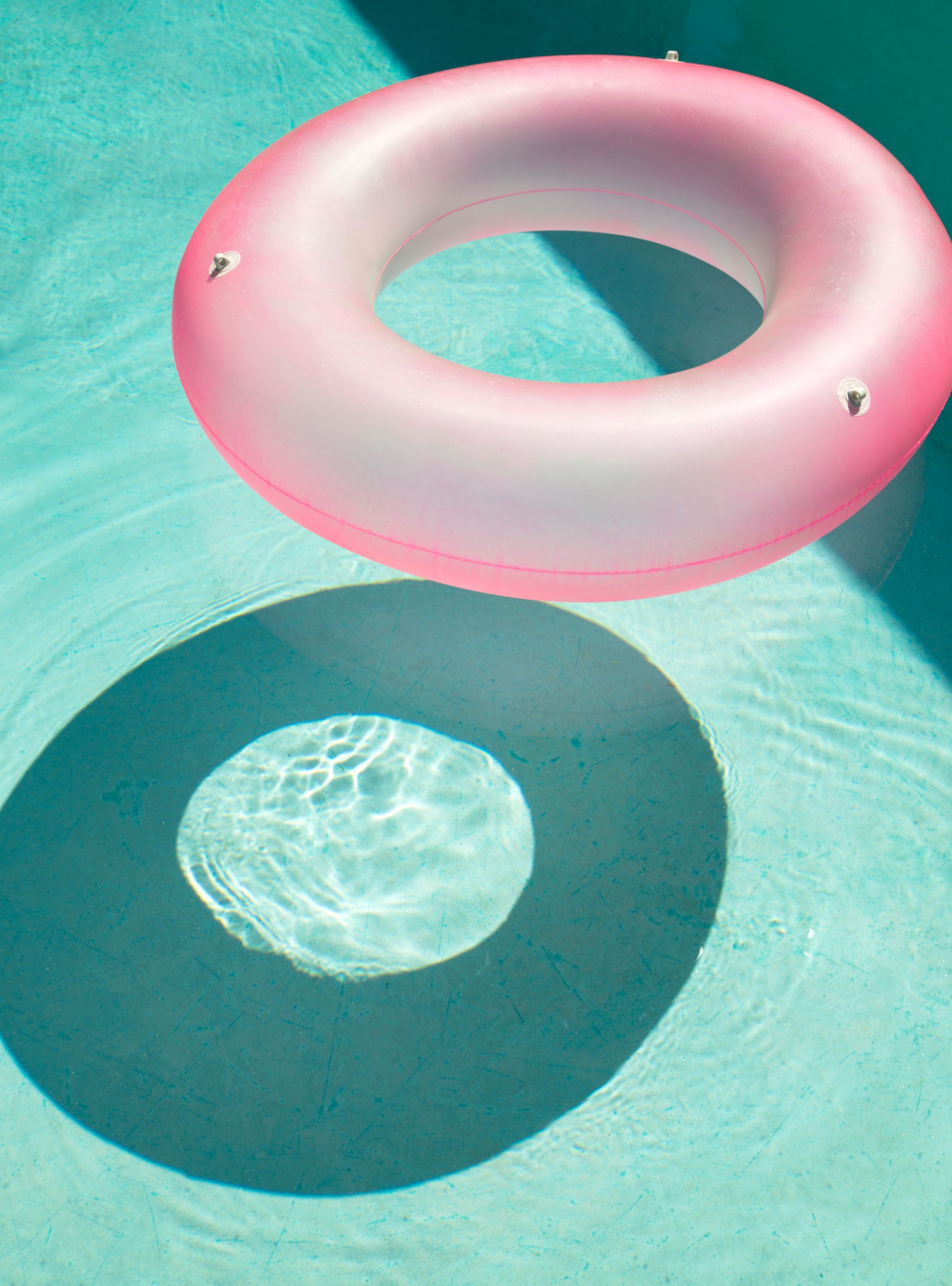 A photo of bright blue pool water with a bright pink inner tube floating in it.