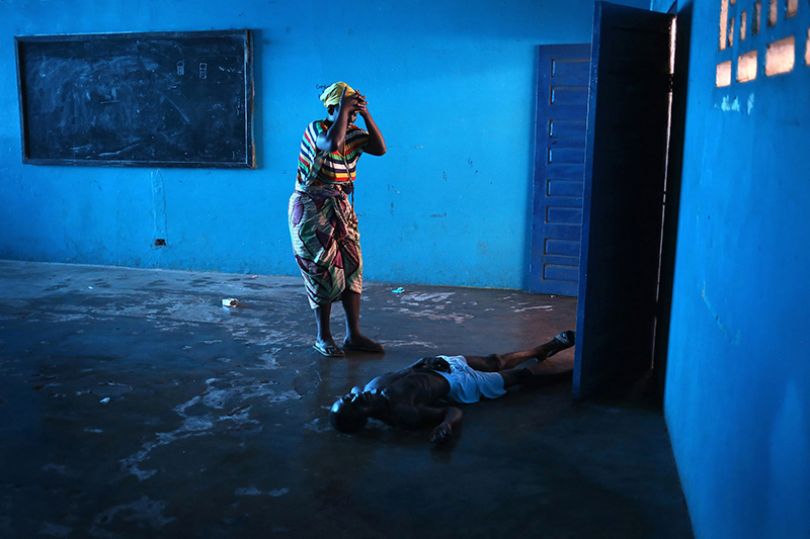 Copyright: John Moore / Getty Images. Omu Fahnbulleh stands over her husband Ibrahim after he fell and died in a classroom used for Ebola patients.