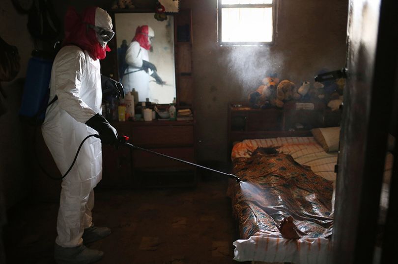 Copyright: John Moore / Getty Images. A burial team sprays disinfectant over the body of a woman suspected of dying of Ebola in her home.