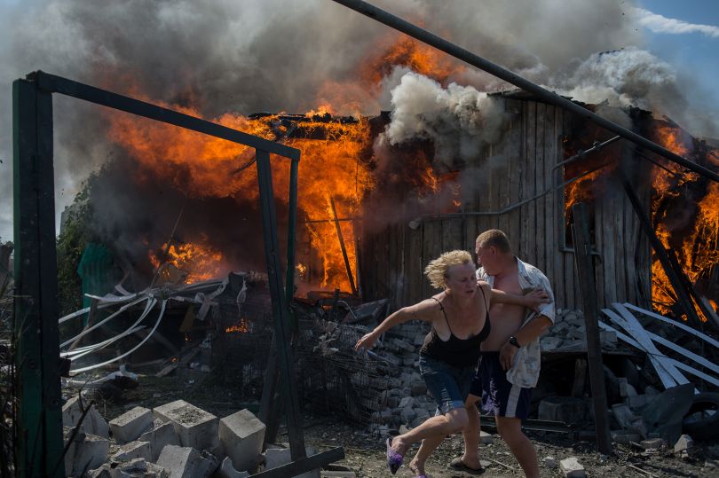 Civilians escape from a fire at a house destroyed by an air attack in Donbass, a village in Luhanskaya, eastern Ukraine, on July 2, 2014. © Valery Melnikov. Photojournalism Single Image Winner, Magnum and LensCulture Photography Awards 2016